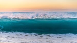 photo of ocean wave coming in, below an orange sunset